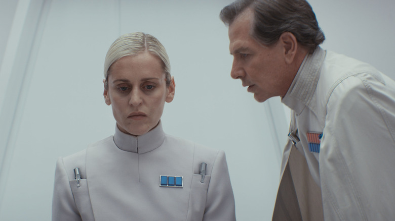 Denise Gough as Supervisor Dedra Meero seated next to Ben Mendelsohn as Director Orson Krennic staring at her imposingly in Andor season 2