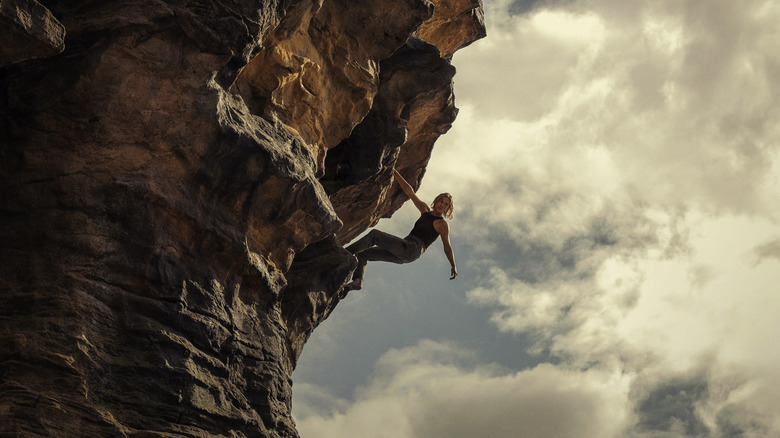 Sasha hangs off a cliff face in Apex