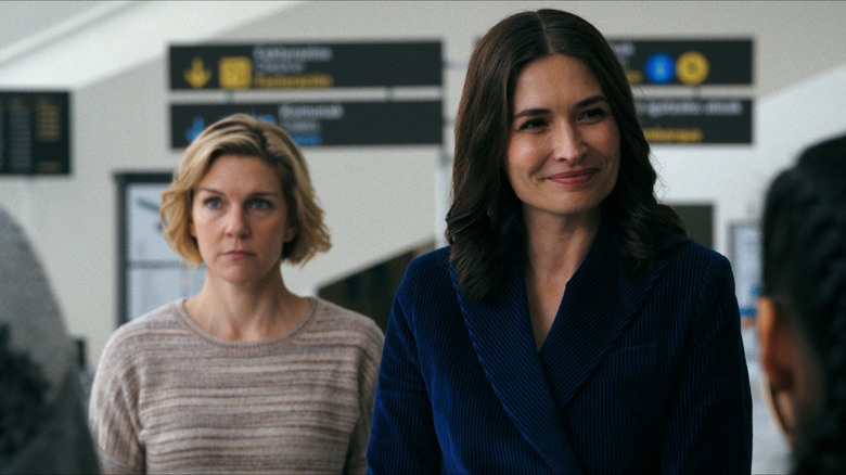 Zosia smiling at people in the airport with Carol scowling behind her on Pluribus
