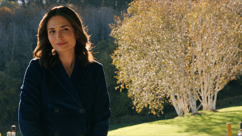 Zosia smiling slightly standing in front of a tree on Pluribus