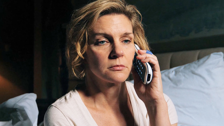 Rhea Seehorn's Carol Sturka sits on her bed while holding a phone to her ear in Pluribus