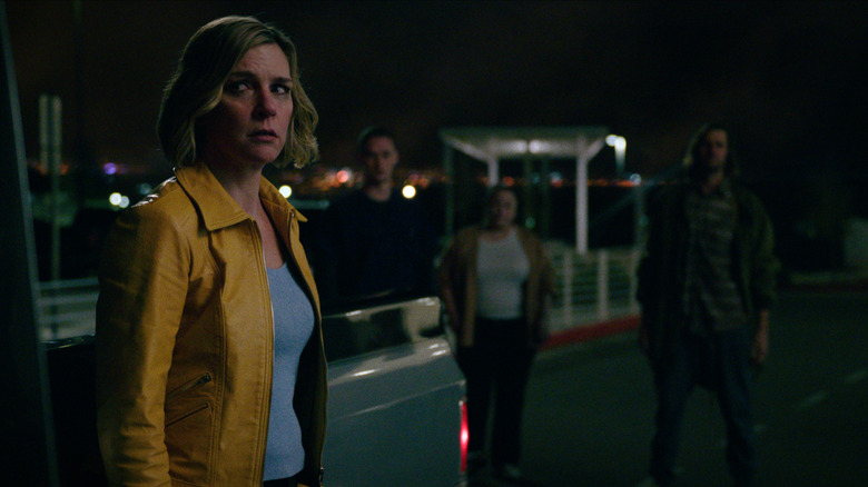 Rhea Seehorn as Carol Sturka looking worried beside a pickup truck with shadowy people in the background in Pluribus