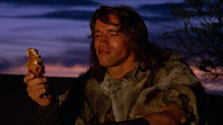 Arnold Schwarzenegger as Conan eating chicken by a fire in Conan the Barbarian