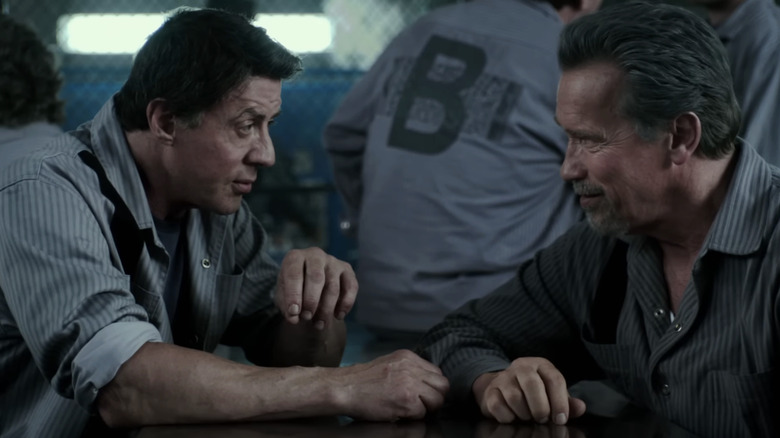 Arnold Schwarzenegger's Emil Rottmayer sits across from Sylvester Stallone's Ray Breslin at a table in a prison in Escape Plan