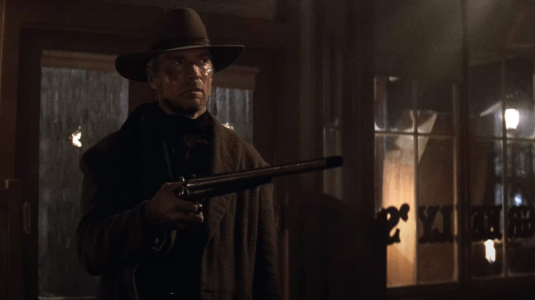 William Munny stands in a bar holding up a long gun
