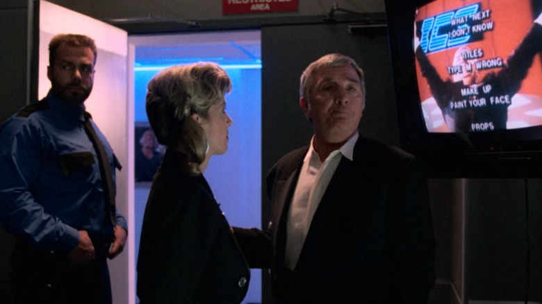 Damon Killian next to a television with joke credits on screen in The Running Man