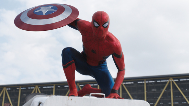 Tom Holland as Peter Parker wearing his Spider-Man suit and holding Captain America's shield in Captain America: Civil War