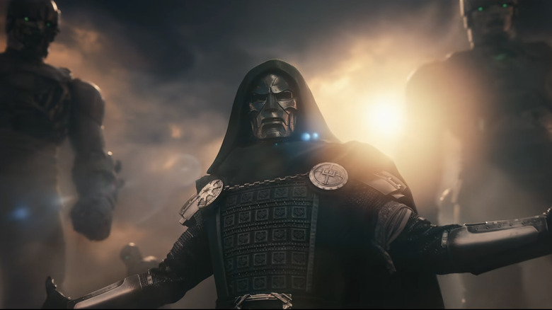 Robert Downey, Jr. as Doctor Doom holding up his arms with two giant Sentinels behind him in Avengers: Doomsday