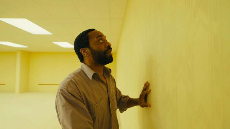 Chiwetel Ejiofor as Clark running his hand against a wall and looking alarmed in an empty office in Backrooms