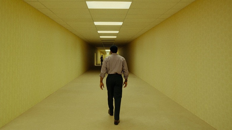 Chiwetel Ejiofor as Clark walking through a long hallway with a shadowy figure at the end in Backrooms