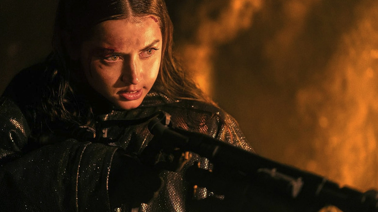Eve holding a flamethrower with light reflecting on her face in Ballerina