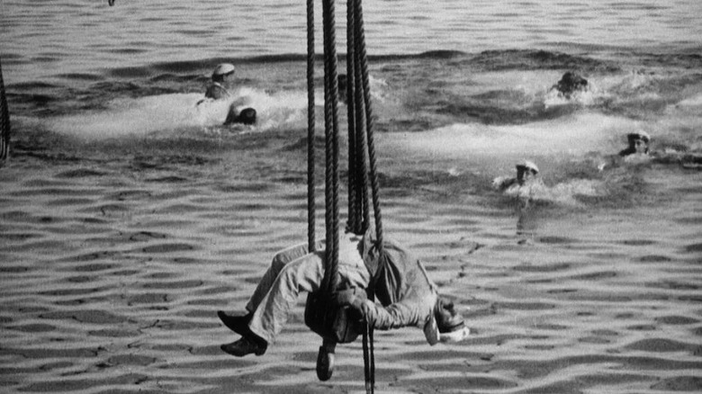 Sailor hanging belly-up on ropes while men at sea look on in Battleship Potemkin