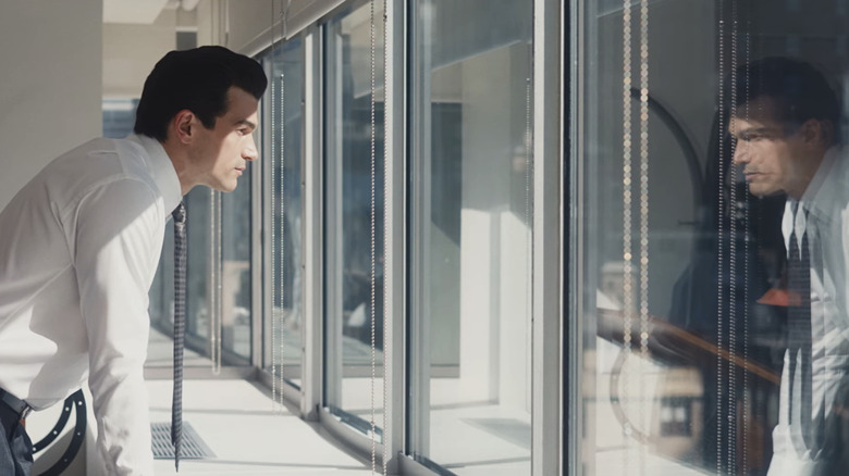 Paul Anthony Kelly as John F Kennedy Jr stands looking out a window in Love Story