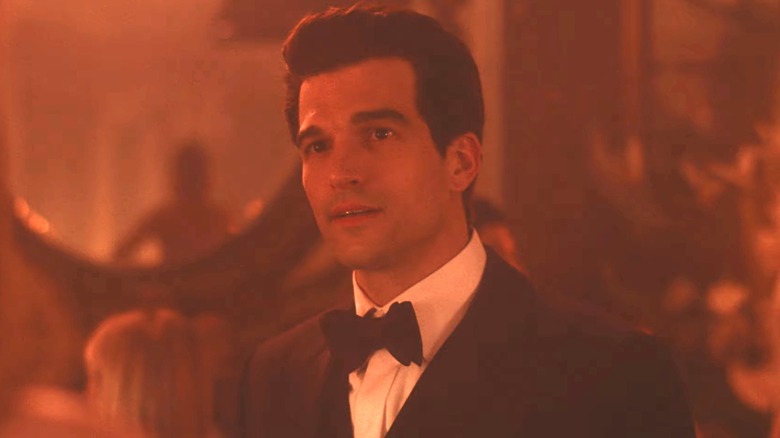 Paul Anthony Kelly as John F Kennedy Jr stands in a room illuminated by red light in Love Story