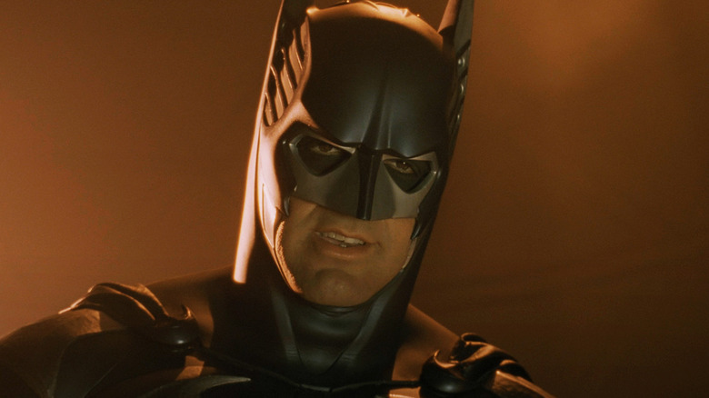 George Clooney as Batman looks down as he stands in front of an orange background in Batman & Robin