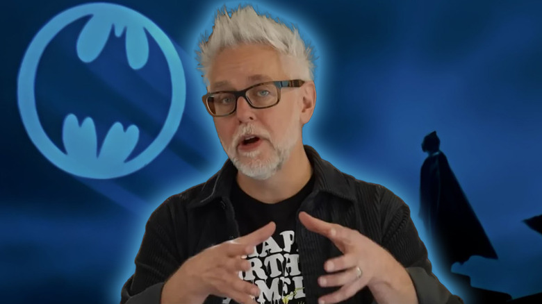 James Gunn gestures against a background showing the bat signal and Michael Keaton's Batman