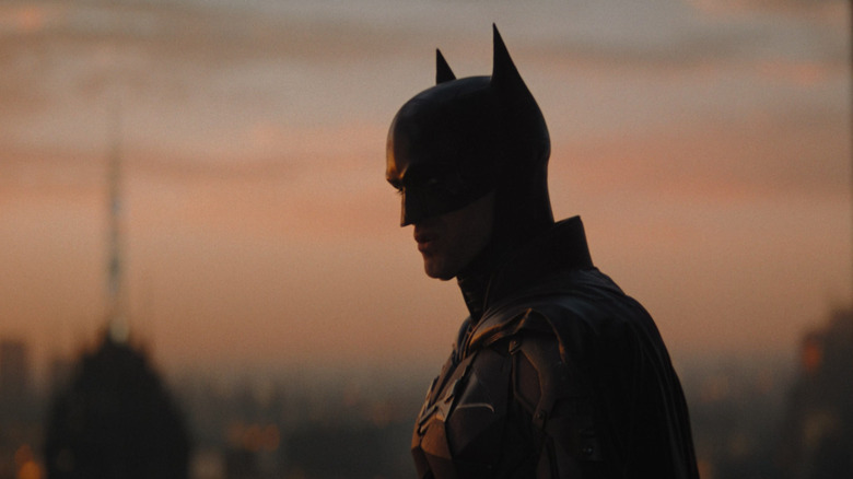 Robert Pattinson's Batman stands against a twlight sky in The Batman