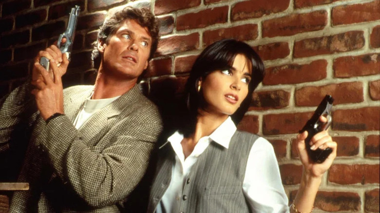 David Hasselhoff and Angie Harmon as Ryan McBride and Mitch Buchannan up against a brick wall with guns drawn in a Baywatch Nights promotional photo