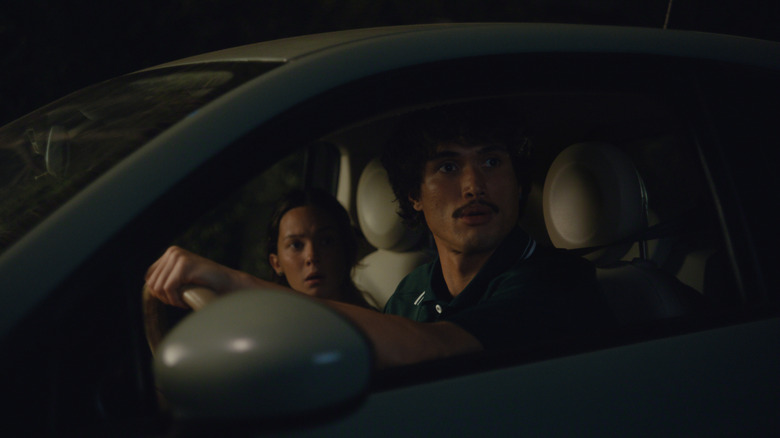Charles Melton as Austin Davis and Cailee Spaeny as Ashley Miller sitting in their car with shocked expressions in Beef