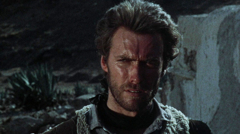 ए फिस्टफुल ऑफ डॉलर्समध्ये रात्रीच्या वेळी बाहेर उभा असताना क्लिंट ईस्टवुडचा मॅन विथ नो नेम क्लोजअपमध्ये दिसत आहे