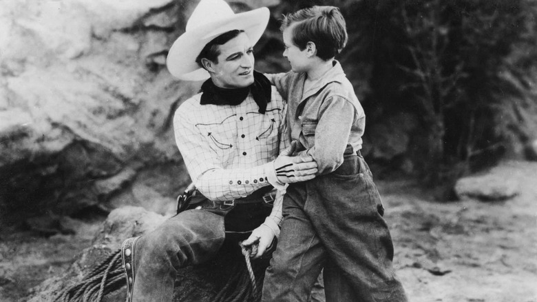 Tom, in his full cowboy duds, comforting a young boy in the 1926 film No Man's Gold.