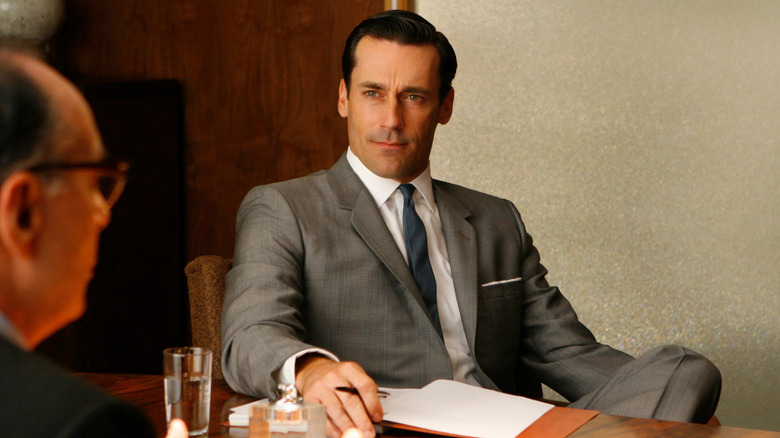 Jon Hamm as Don Draper sitting at a table in Mad Men