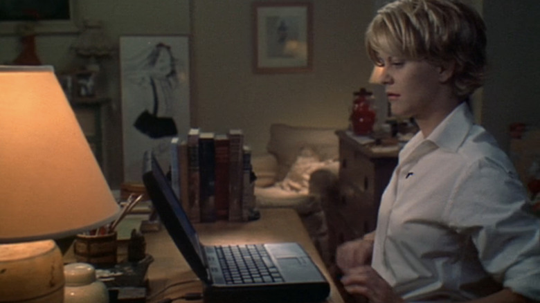 Meg Ryan's Kathleen Kelly sits at her desk looking at her laptop in You've Got Mail