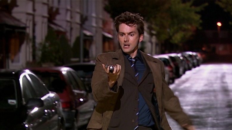 The Doctor, holding a widget in his hand, running down a street, in Doctor Who