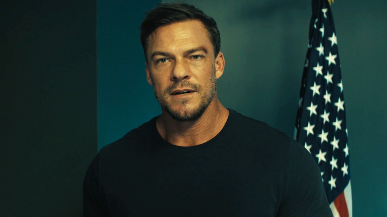 Alan Ritchson's Jack Reacher stands in front of a US Flag in Reacher