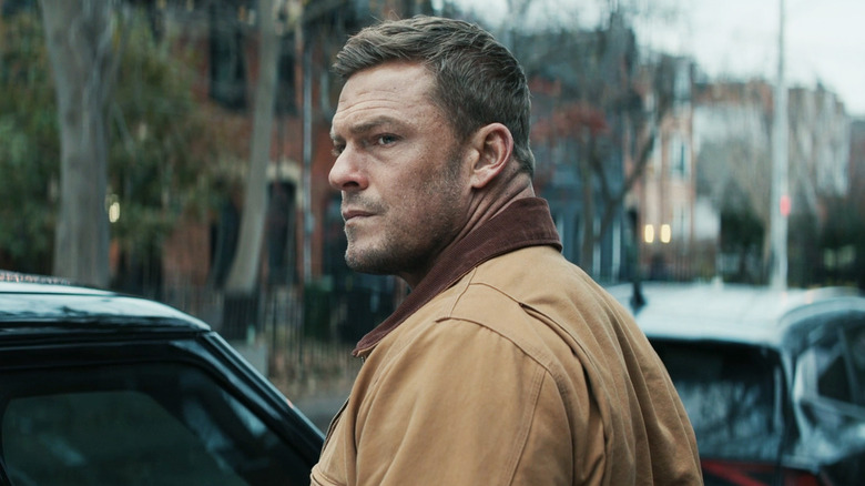 Alan Ritchson as Jack Reacher looks off into the distance while standing on a New York street in Reacher