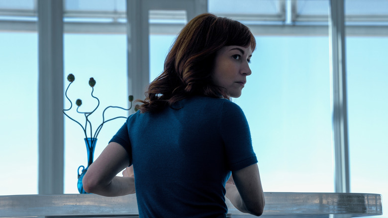 Helena sits at the table and looks back back over her shoulder