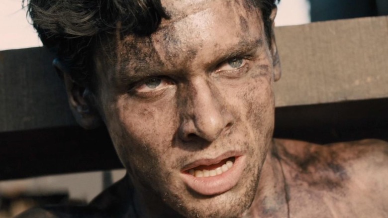 Jack O'Connell as Louis "Louie" Zamperini in Unbroken with wood over his shoulders and covered in dirt