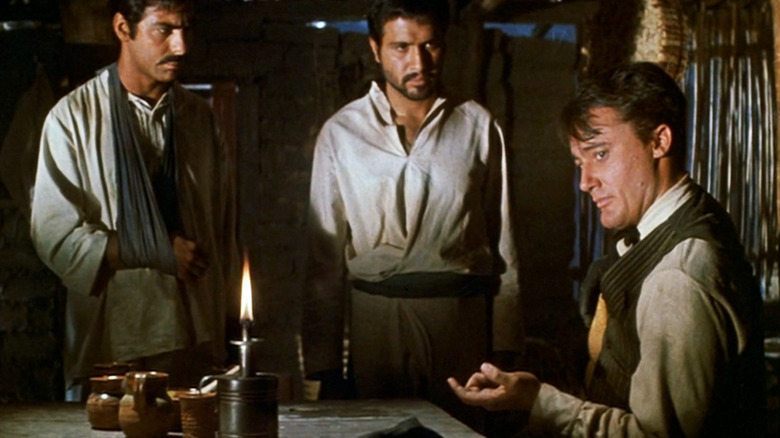 Robert Vaughn's Lee sits at a table as two men watch in The Magnificent Seven