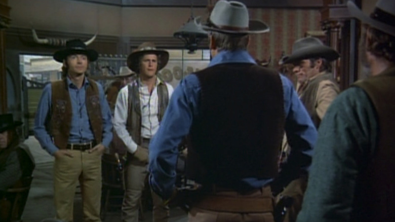 Pete Duel's Hannibal Heyes/Joshua Smith stands beside  Ben Murphy's Kid Curry/Thaddeus Jones as they confront Lee Majors' Joe Briggs in a saloon in Alias Smith and Jones