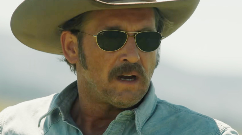 Josh Lucas' John Dutton wearing sunglasses and a cowboy hat outside while looking alarmed in Yellowstone
