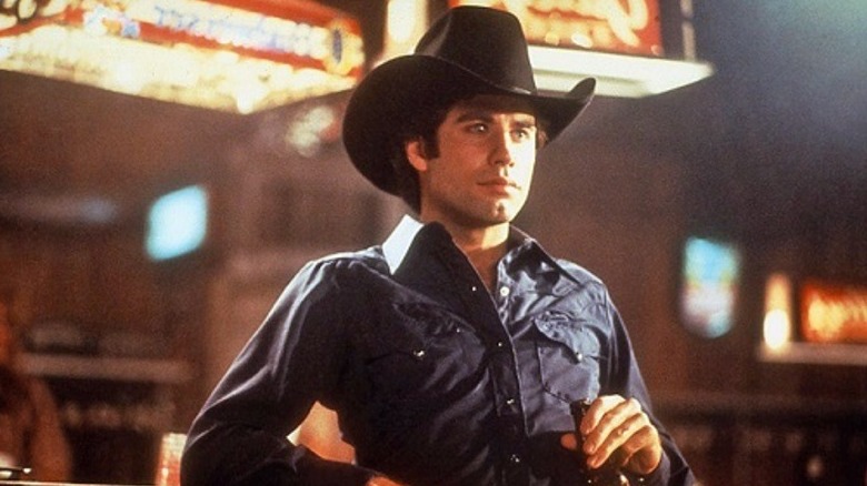 Bud Davis (John Travolta) holds a beer while leaning against a bar in Urban Cowboy
