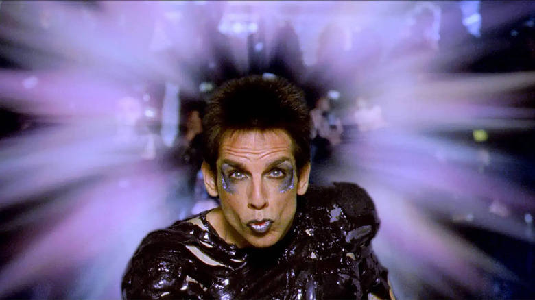 man in purple makeup pursing his lips in front of a purple lens flare