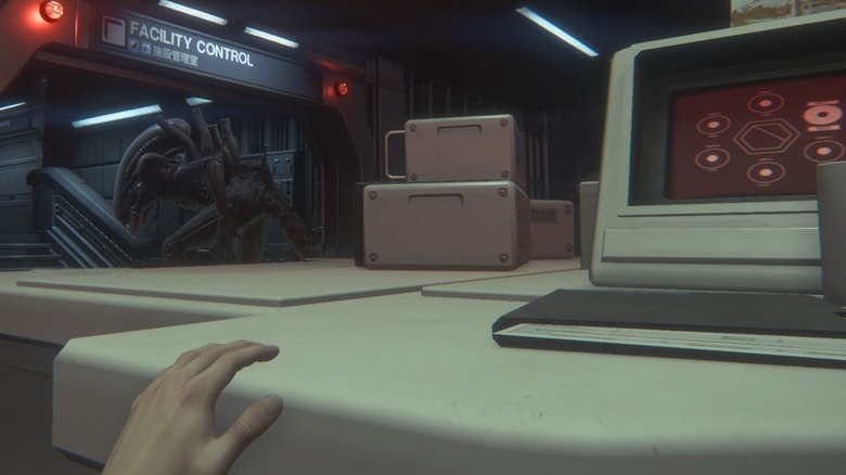 Amanda cowers behind a desk, as the xenomorph passes by