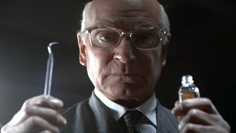 Marathon Man - Christian Szell holding dentistry tool in one hand and clove oil bottle in other