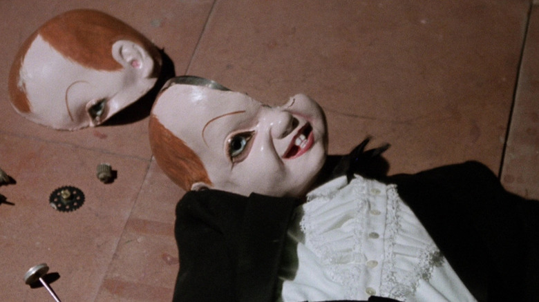 A broken porcelain doll grins blankly upwards in Deep Red
