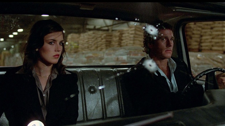 The Player (Isabelle Adjani) and the Driver (Ryan O'Neal sit in a sedan with bullet holes in the windshield in The Driver