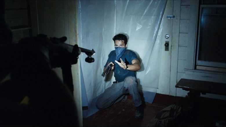 A gun pointed at Christopher Abbott as Will in It Comes At Night, squatting on the floor with a bandana over his face