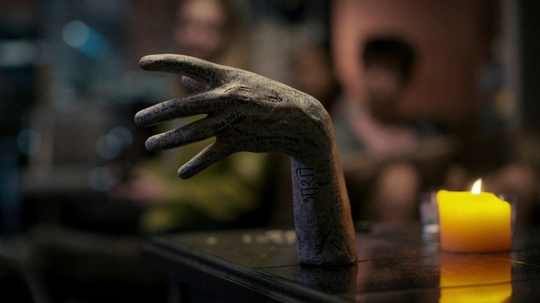 The plaster, graffiti-covered hand from Talk to Me, sitting in front of a stubby candle