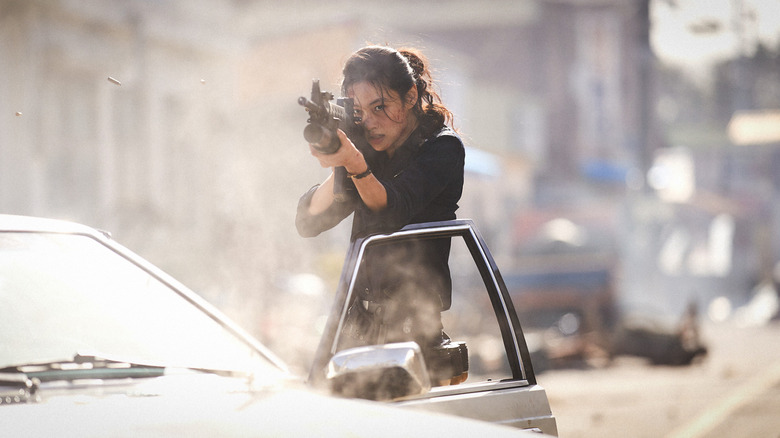 Hoyeon as Sung-ae holding up a weapon and firing from behind the door of a cop car in Hope