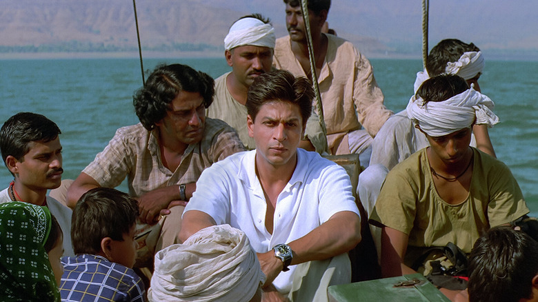 Shah Rukh Khan as Mohan dressed in white sitting on small boat alongside other men in Swades