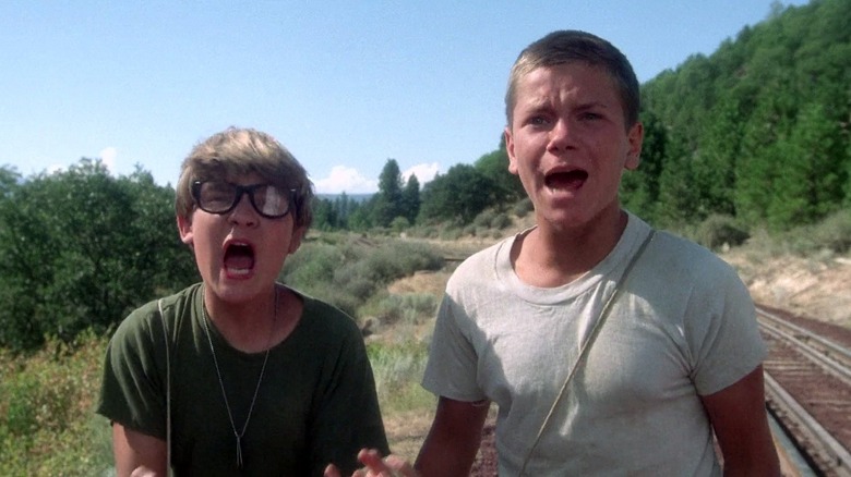 River Phoenix as Chris Chambers and Corey Feldman as Teddy Duchamp in Stand By Me, standing outside by the train tracks, looking toward the camera and screaming.