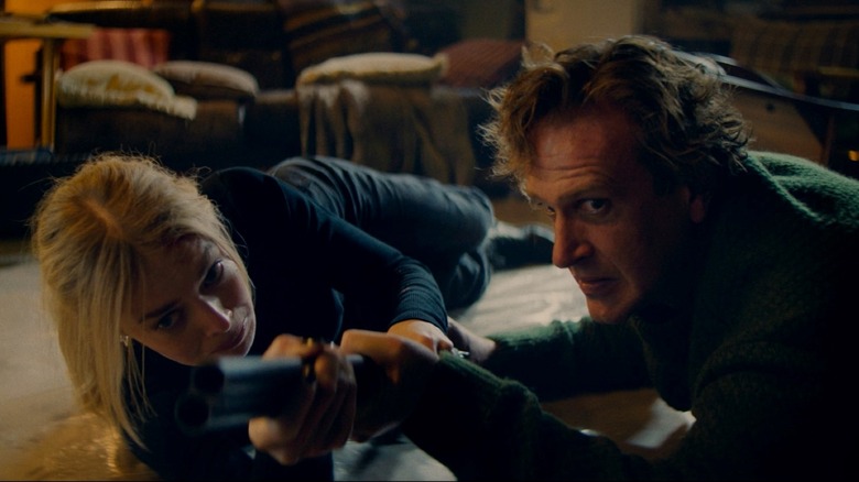 Samara Weaving as Lisa and Jason Segel as Dan fighting over a shotgun on the floor of a cabin in Over Your Dead Body