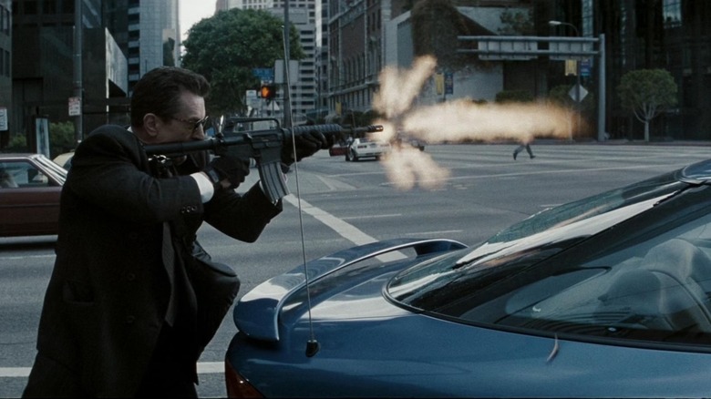 Neil McCauley (Robert De Niro) fires an assault rifle behind a car in the street in Heat (1995)
