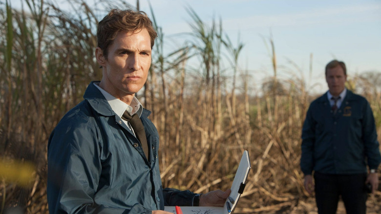 Rust Cohle (Matthew McConaughey) reviews his notes in a grassy field with Marty Hart (Woody Harrelson) in True Detective