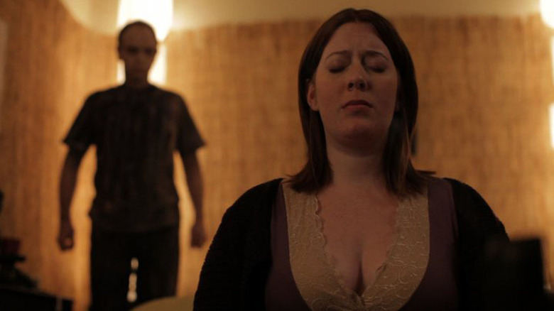 Tricia (Courtney Bell) sitting with her eyes closed in front of out-of-focus creepy man in Absentia